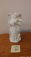 Front view of white ceramic angel holding violin as a candlestick holder, showing detailed wings and robe folds
