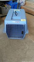 Blue plastic animal crate with metal wire door facing forward on concrete floor