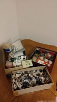 Three boxes on a wooden surface holding assorted buttons including big, little, fancy, and plain styles