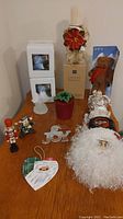 Full view of Christmas decorations on table including boxed illuminated angels, candle holder, teddy bear, Santa face, and assorted ornaments.