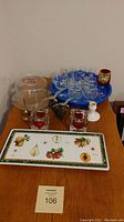 View of covered cheese tray, blue tray with 8 shooter glasses, 4 brandy snifters, 2 heart-shaped votive holders, and rectangular fruit platter