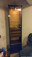 Full view of tall glass front cabinet with light on inside, showing closed door, glass shelves, and drawers