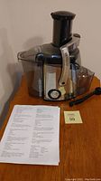 Full view of Juiceman juicer on wooden surface with accompanying juicing recipes sheet and plastic pusher tool.