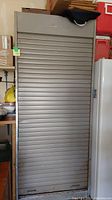 Closed view of the tall, grey metal cabinet with a roll-up shutter door.
