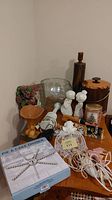 Photo showing various household items including tall glass vase, kissing angels figurines, mirror with flowers, pie and cake divider, glue tool, electric scissors, punch bowl with ladle, ice bucket with tongs, Christmas tin, golf club business card holder, and some cords.
