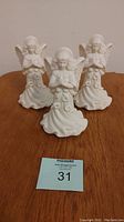 Front view of three white Partylite praying angel candlestick holders showing detailed praying angel figures about 7 inches tall.