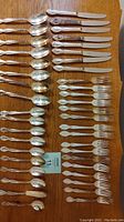 Top-down photo of cutlery pieces laid out in rows showing spoons, knives, and forks with a card in the middle.
