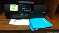 SiriusXM docking station with radio unit inside, plus user manuals laid out on a wooden surface