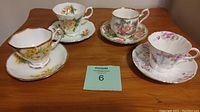 Four Royal Albert bone china tea cups and matching saucers arranged on wooden table showing floral patterns and gold trim