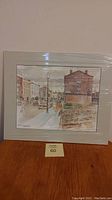 Photo of unframed artwork with white mat showing a street scene with buildings and lamp posts on Walton Street, Port Hope.