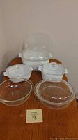 Photo showing front view of six casseroles including three white Corningware casseroles with lids and two glass casseroles with lids plus a plastic lid.