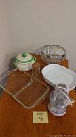 Multiple kitchen items on wood surface including casserole dishes, salad bowl, small casserole with lid, glass jar, and chopper shown separately