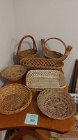 Photo showing set of seven wicker baskets of various shapes and sizes arranged on wooden surface.