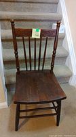 Photo of a single wooden chair with a dark finish, vertical spindle backrest, and slightly curved seat.