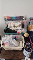 Overview of pens, pencils, glue, markers, Sharpies, and tape in baskets and containers with owl-patterned pouch and a blue plush toy partly visible.