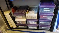 Photo of multiple labeled plastic storage containers stacked on shelves containing various crafting supplies such as sequins, beads, lapel pins, blades, cutters, needles, threaders, sculpting tools, knitting and crocheting supplies.