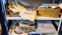 Shelf stacked with folded fabric pieces, baskets, and plastic bags containing needlework supplies