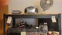 Wide shot showing multiple electronics on shelving including a portable CD player, fan, various headphones and other devices