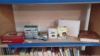 Photo showing shelf with all items: tin train set, puzzle box, Bob Ross item, ancestry DNA kit, owl notebook, and small accessories.