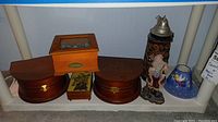Shelf view showing all items: two wooden music boxes, smaller wooden box, ceramic beer stein with pewter lid, Santa Claus figurine, and painted candle shade.
