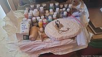 Overview of multiple bottles of craft paint, white pipe cleaners, wooden crafts, and ceramic Native American woman figure on oval base.