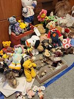 Wide view showing assorted plush and beanie bears including Snoopy, knitted scarecrow, flower plush, light brown teddy bears and other character dolls, all on a carpeted floor with wooden furniture in background.