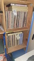 Photo showing wooden shelf holding a large selection of vinyl LP records and two box sets titled The Magical World of Melody and Remembering the 60s on top.