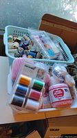 Assorted thread spools and skeins in a white basket and on a tabletop showing various colors and brands.