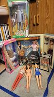 Photo of the lot showing Wizard of Oz Tin Man boxed figure, Elvis & Barbie collector tin box, Victorian Barbie boxed doll, Arctic Barbie boxed doll, and three loose Barbie dolls on floor.