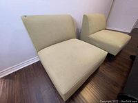 Two large green fabric chairs with cushioned seats and backs, armless, with low wooden legs, placed on wood flooring.