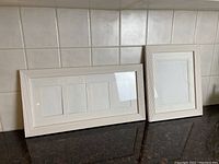Two white picture frames on black surface against tiled background. Larger frame holds three photos, smaller frame holds one photo.