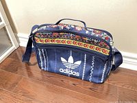 Front view of Adidas laptop bag showing floral and striped pattern and Adidas trefoil logo on navy background.