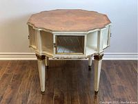 Front view of octagonal wooden antique table with cream color, glass panel doors with metal grille, and detailed leg carvings