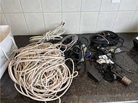 Wide view of the lot showing multiple long white CAT6 Ethernet cables on the left and various black cables, adapters, and connectors on the right on a kitchen counter.