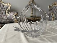 Clear glass swan-shaped serving bowl with handle on table with patterned upholstery in background.