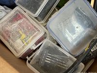 Image showing multiple plastic containers and toolboxes filled with assorted small tools and hardware pieces such as screws and nails. Dust visible on container surfaces.