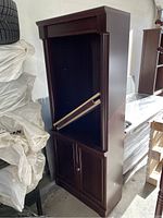 Full view of tall dark wood book shelf with two cabinet doors at the bottom, shelves missing, in garage with tires and other items around.