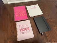 Four notebooks arranged on a wooden floor, showing front covers with colorful text designs.