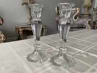 Pair of clear glass upright candle holders on a table with decorative background.