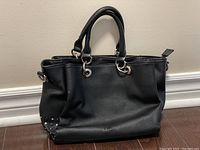 Front view of black leather purse showing structure, handles, and studded corner detail.