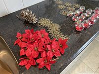Close-up of clear plastic ornaments filled with artificial flowers and gems, gold sparkle snowflakes, red poinsettias, and large glittered pinecone displayed on countertop.