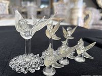 Six crystal bird figurines arranged on a black cloth, one larger bird on a textured crystal base with five smaller birds around it.