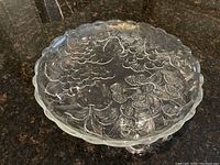 Top-down view of clear glass serving dish showing detailed raised fruit pattern and scalloped edges.