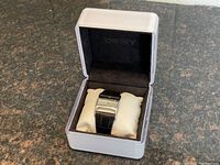 DKNY women's wrist watch displayed on a cream-colored pillow inside a white box with black interior lining.