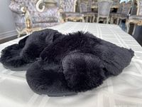 Side angle view of one black fuzzy slipper showing soft plush material and rubber sole.