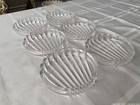 Six clear round glass drink coasters arranged on a white fabric surface, showing the ribbed pattern and scalloped edges.
