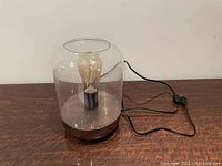 Full view of the large table lamp showing glass top, wood base, power cord, and Edison bulb.