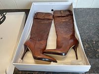 Pair of brown Nine West boots in original box with visible woven design on shaft and buckle strap near top.