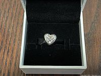 Close-up image of the heart-shaped Pandora charm inside a black velvet-lined white box.