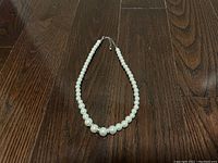 Photo of faux pearl necklace laid flat on dark wood surface showing bead sizes and silver clasp.